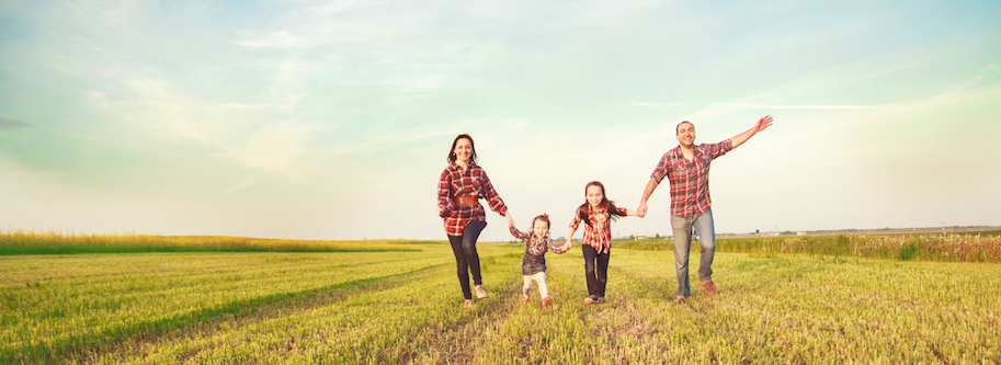 Healthy family of four happily holding hands while walking across a field